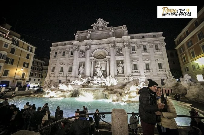 La Fontana de Trevi iluminada de noche con visitantes en la plaza