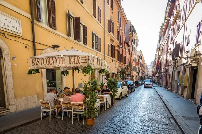 Una calle romana empedrada con edificios ocres y un café